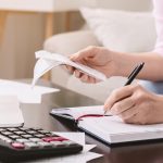 Mature lady with bills noting her purchases at home