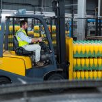 Factory worker loading packed juice bottles on forklift