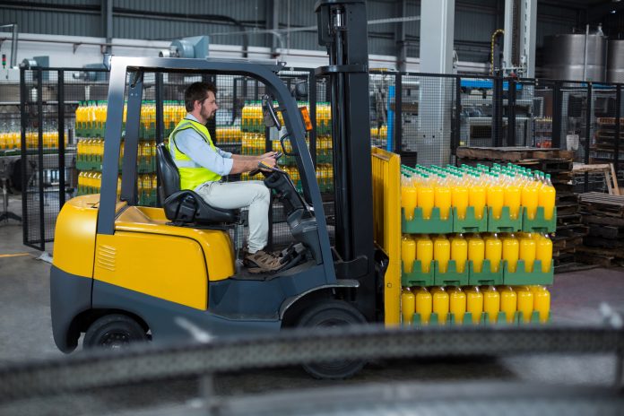 Factory worker loading packed juice bottles on forklift